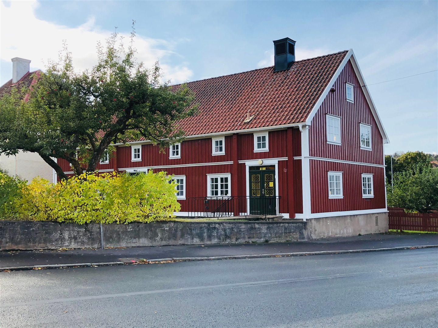 Rødt svensk trehus med hvite vinduskarmer, tegltak og grønn hage.