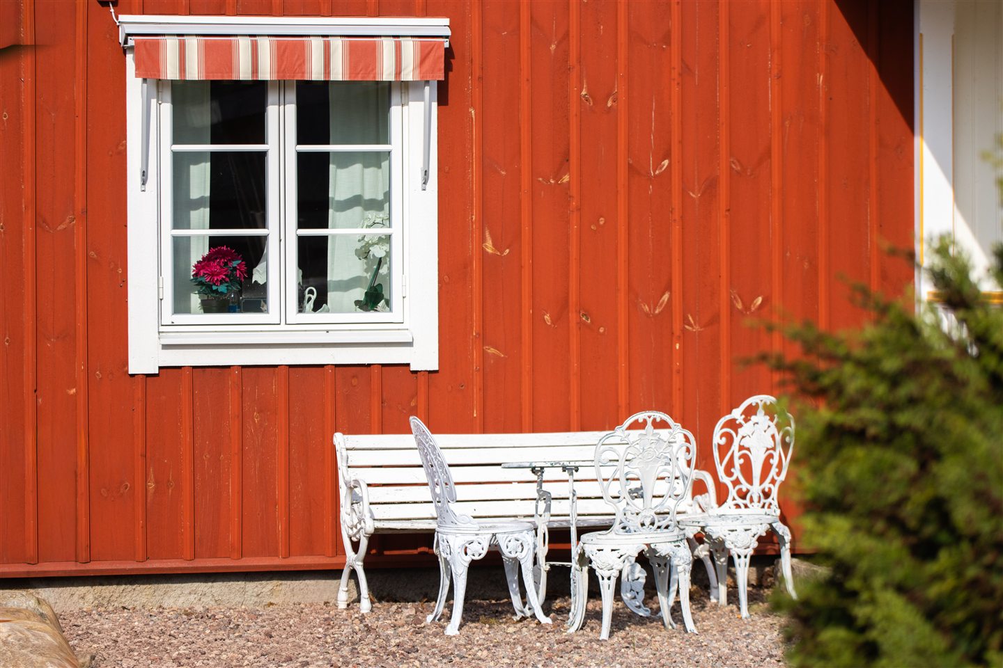 Hvite hagemøbler foran en rød svensk trevegg med vindu og markise.